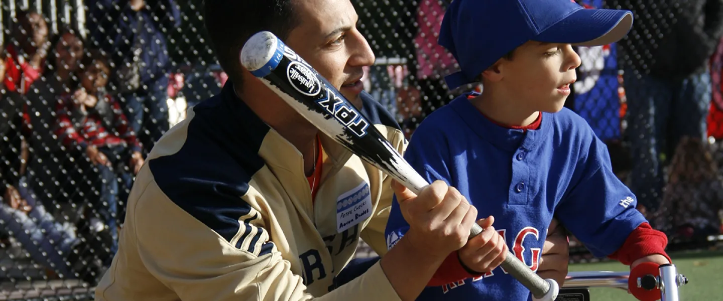 Dad helps a kid play baseball on a baseball field