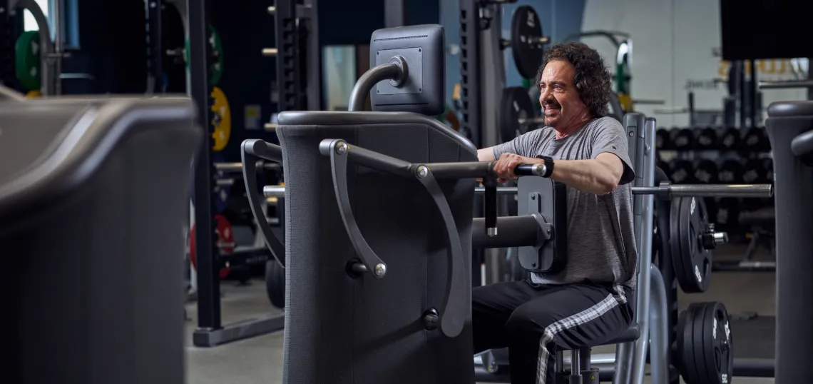 EGYM marketing image, older man using the EGYM arm machine, he is inside a gym with other equipment behind him.